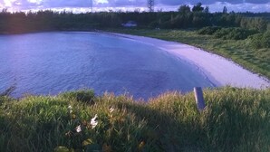 Una playa con una orilla curva, zonas de césped y una torre de líneas eléctricas a lo lejos.