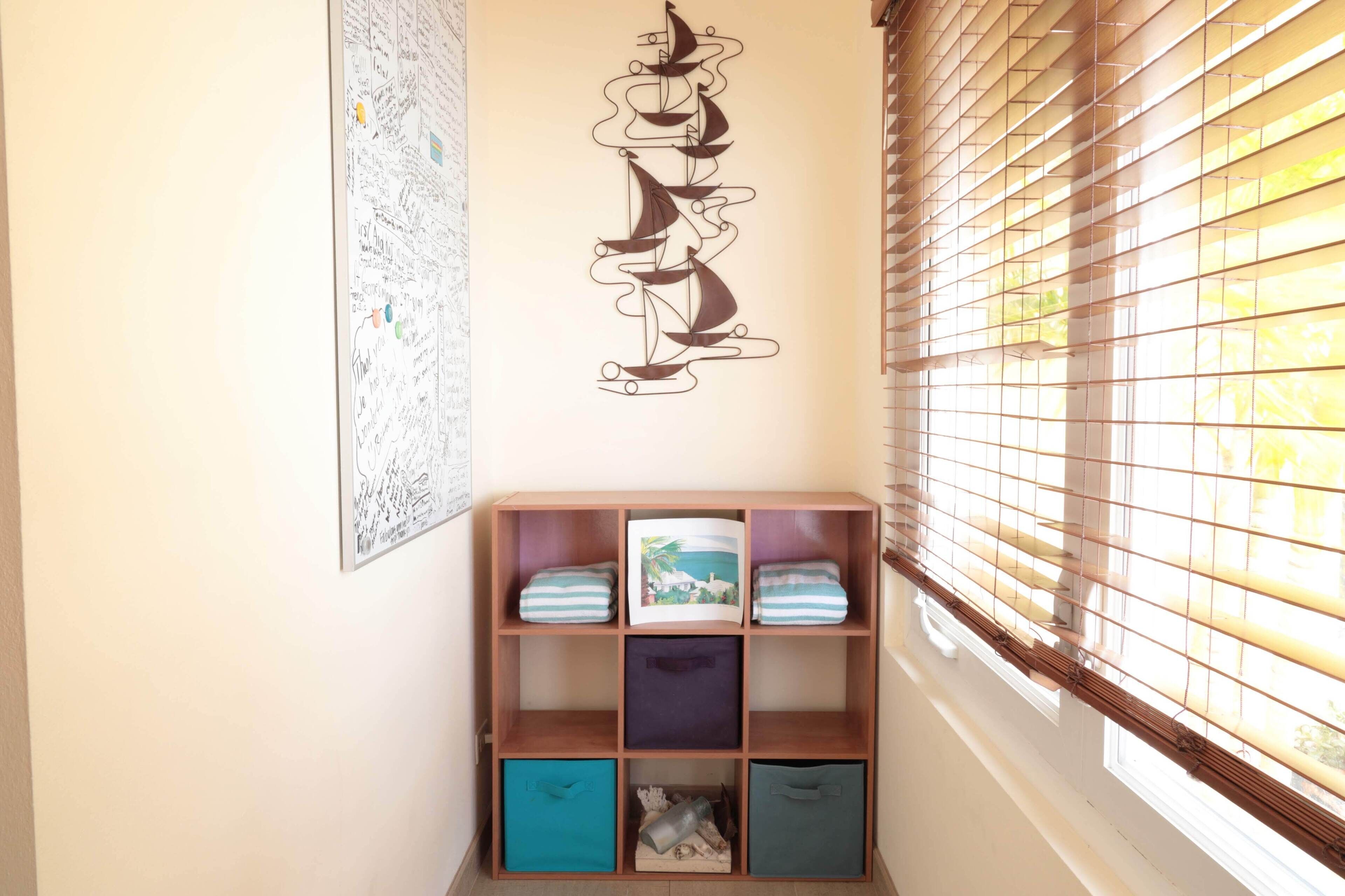 A corner of a room with a wooden bookshelf, a wall with a decorative abstract art piece, and a window with blinds.