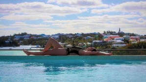 Una persona recostada en una silla de piscina con vistas a un pueblo costero y un cielo despejado.