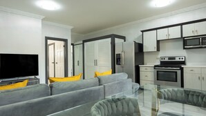 A modern living room with a grey sofa, yellow cushions, a glass coffee table, and a flat-screen TV. - Furnished 1 bedroom Apartment in Gated Complex  (Kingston)