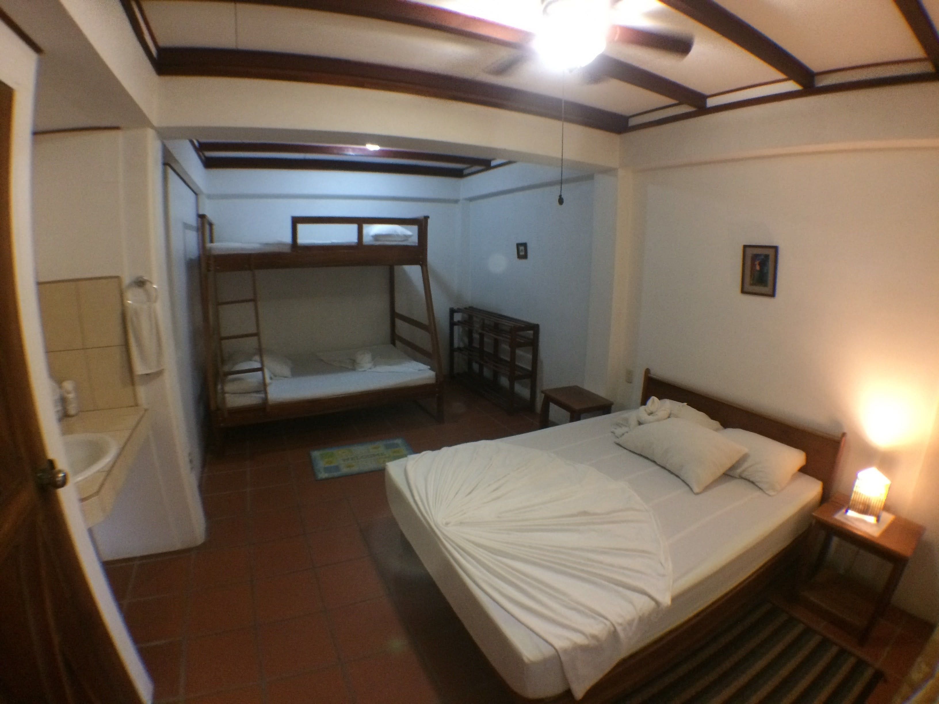 A compact room with a bunk bed, a single bed, a small table, and a bedside lamp.