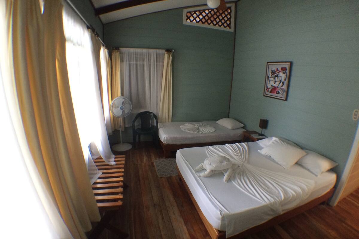 A room with two beds, a fan, a chair, and a window with curtains.