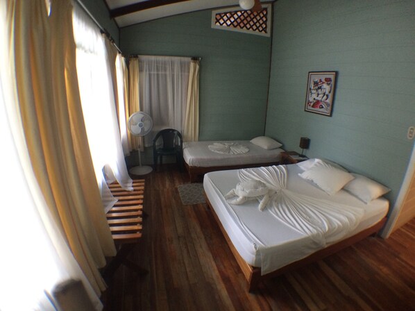Una habitación con dos camas, un ventilador, una silla y una ventana con cortinas.