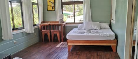 Una habitación con cama, escritorio y silla. Hay una ventana con cortinas, un cuadro en la pared y un equipo de aire acondicionado.