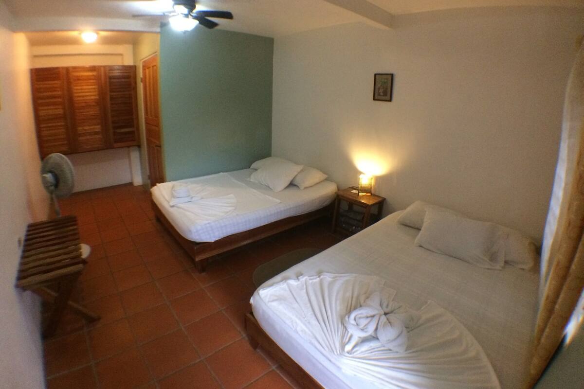 A hotel room with two beds, a ceiling fan, a bedside lamp, and a small table.