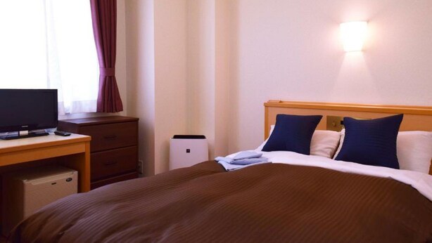 A hotel room with a bed, a desk, a television, and a wall-mounted light fixture. - All In Stay Hakodate (Hakodate)