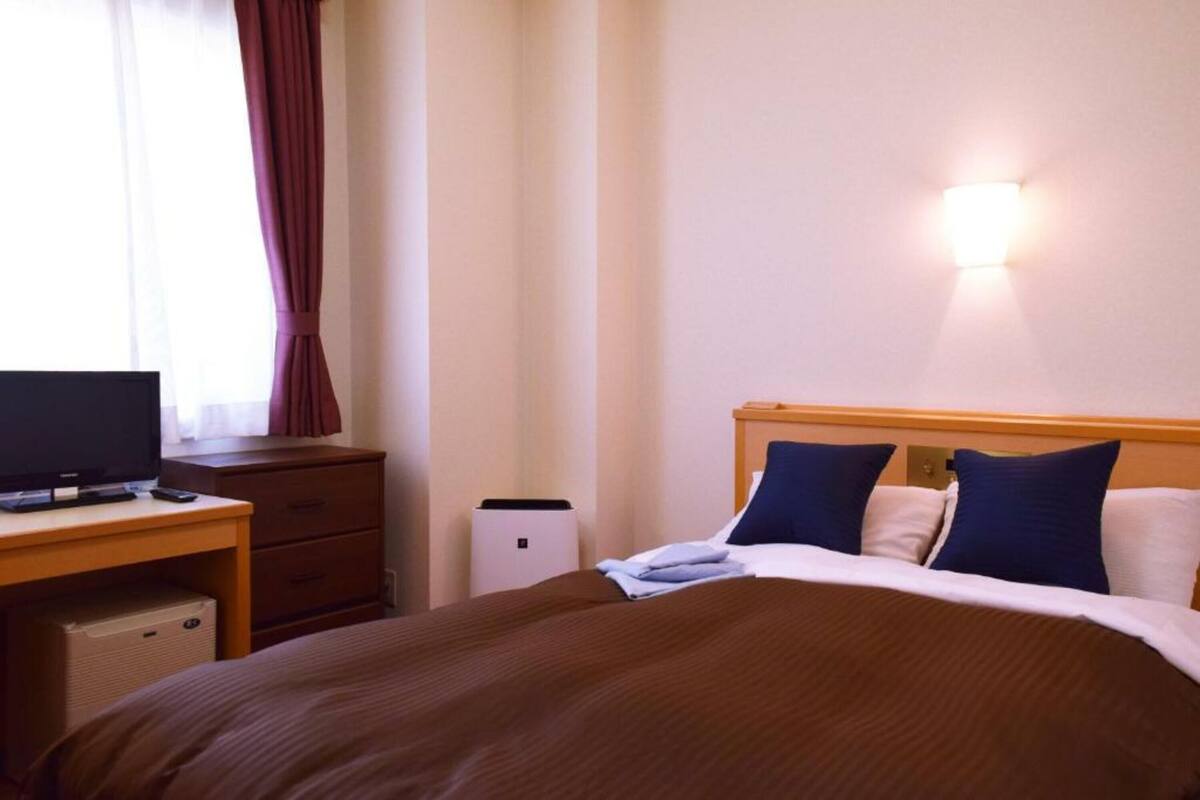 A hotel room with a bed, a desk, a television, and a wall-mounted light fixture.