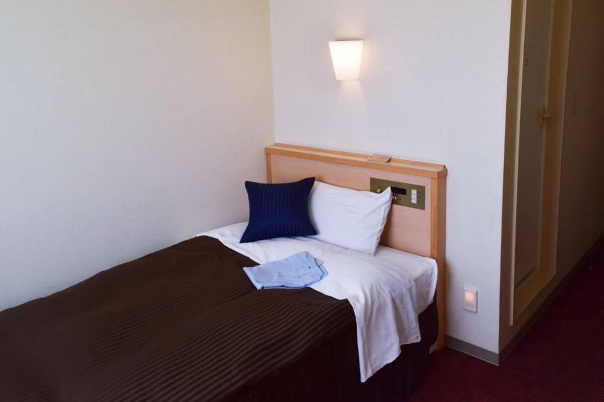 A single bed with a wooden headboard, a white and blue pillow, and a brown blanket.