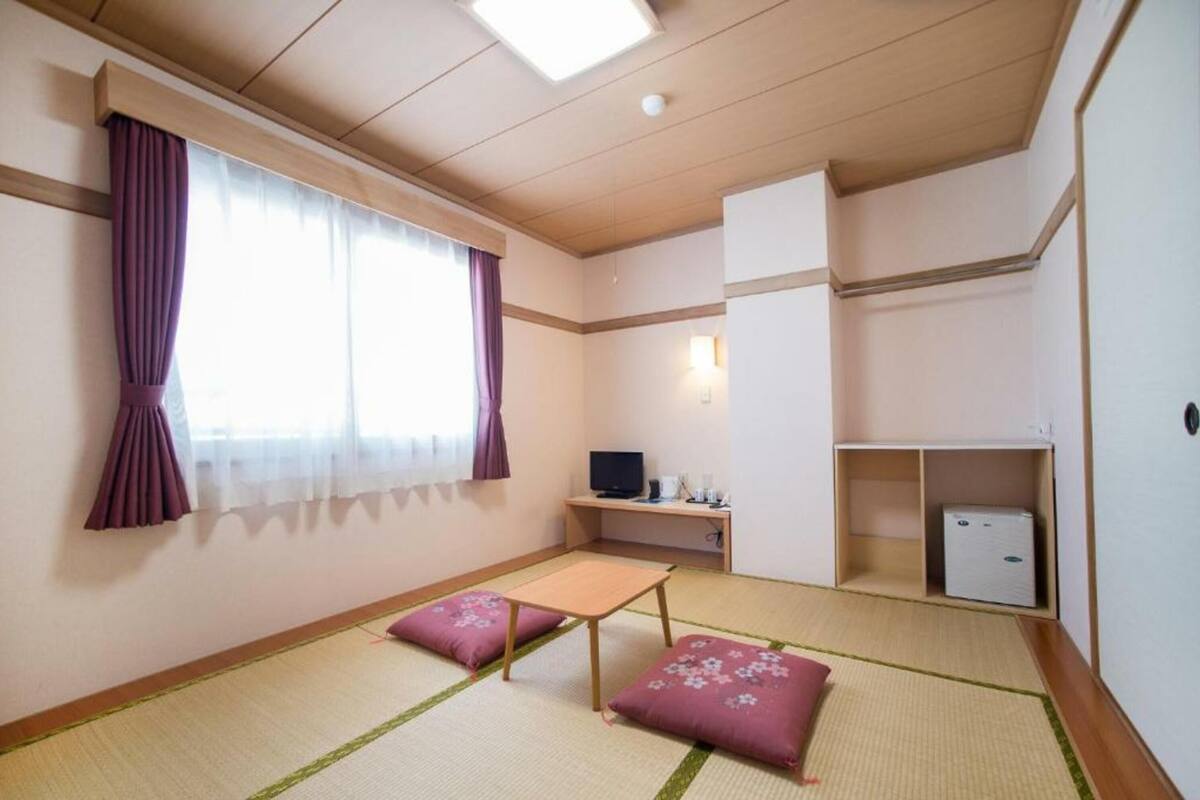 A room with tatami flooring, a futon bed, a television, a desk with a computer, and a wardrobe.