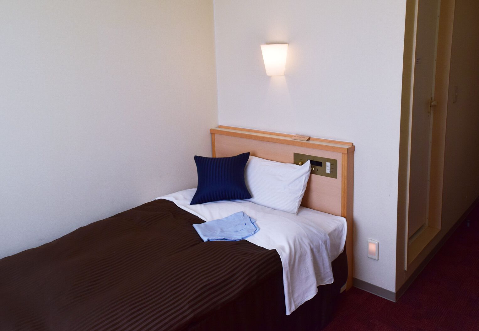 A single bed with a wooden headboard, white bedding, a blue pillow, and a brown blanket.