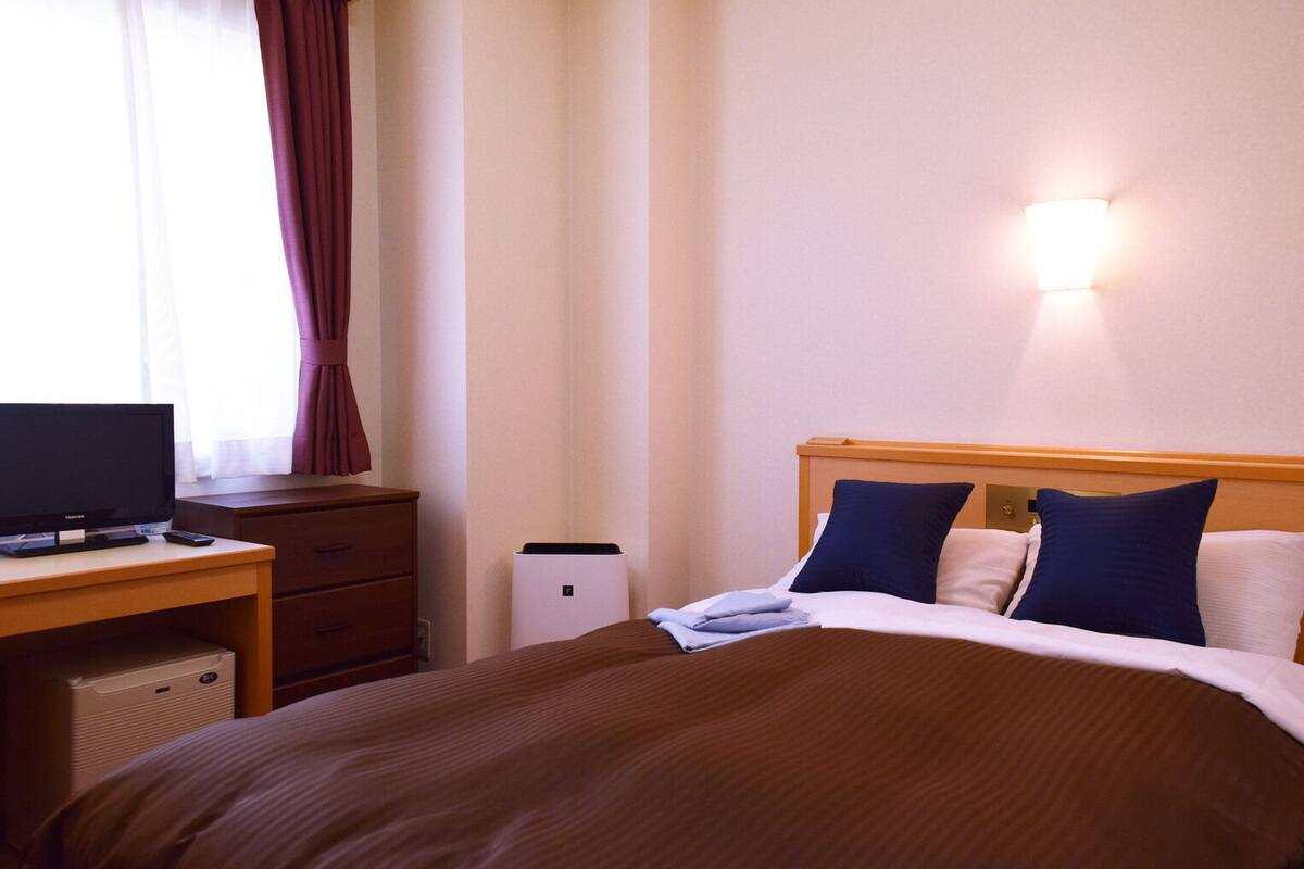 A hotel room with a bed, a desk with a computer, a television, and a wall-mounted light.