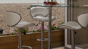 A dining area with a glass table set for two, overlooking a beach. - Bella Vista is a Stunning Beachfront Apartment with 200 5 star reviews (East Preston)