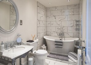 A modern bathroom with a freestanding bathtub, a large mirror, and a marble-tiled wall. - Bella Vista is a Stunning Beachfront Apartment with 200 5 star reviews (East Preston)