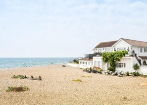 Une propriété située en bord de mer, avec un grand bâtiment blanc, une terrasse dotée de chaises longues et une vue sur la mer.