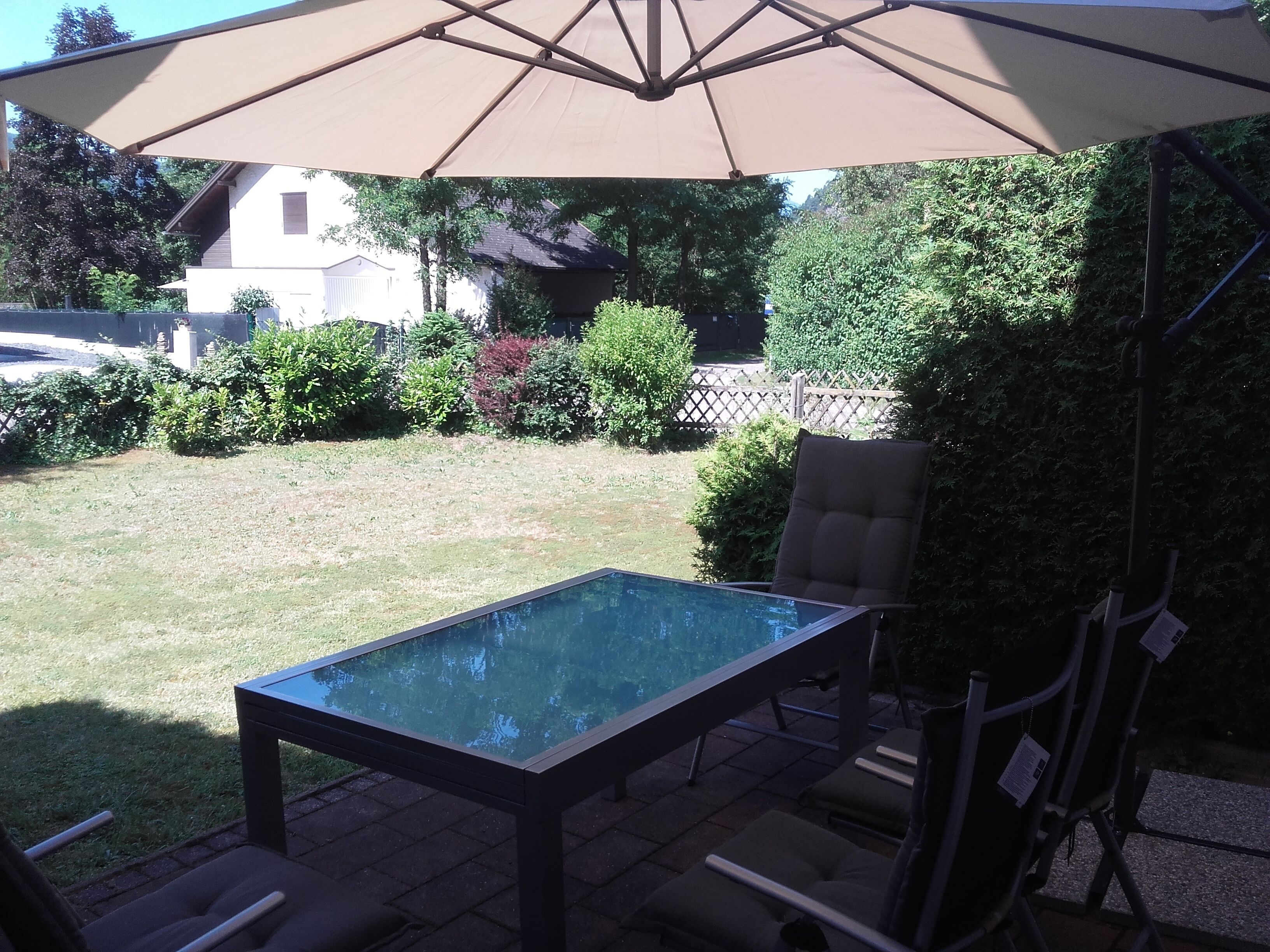 Une terrasse extérieure avec une table à plateau en verre, deux chaises et un grand parasol.