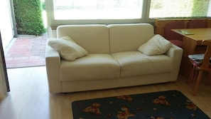 Un canapé beige avec deux coussins, une table à manger en bois avec des chaises et un tapis à motifs.