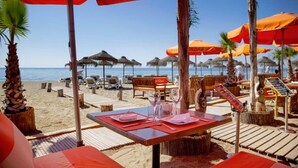 Een restaurant aan het strand met terras, tafels en parasols.