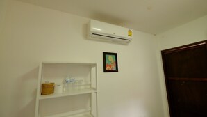 A white wall with a white shelf holding water bottles, a framed picture, and an air conditioning unit. - Patty's Secret Garden (Ko Lanta)