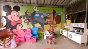 A children's playroom with a large cartoon mural, storage bins, a small kitchen set, and a pink tricycle. - Patty's Secret Garden (Ko Lanta)