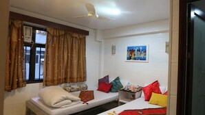 A room with two beds, a ceiling fan, a window with curtains, and a painting on the wall. - Om Guest House (Kowloon)