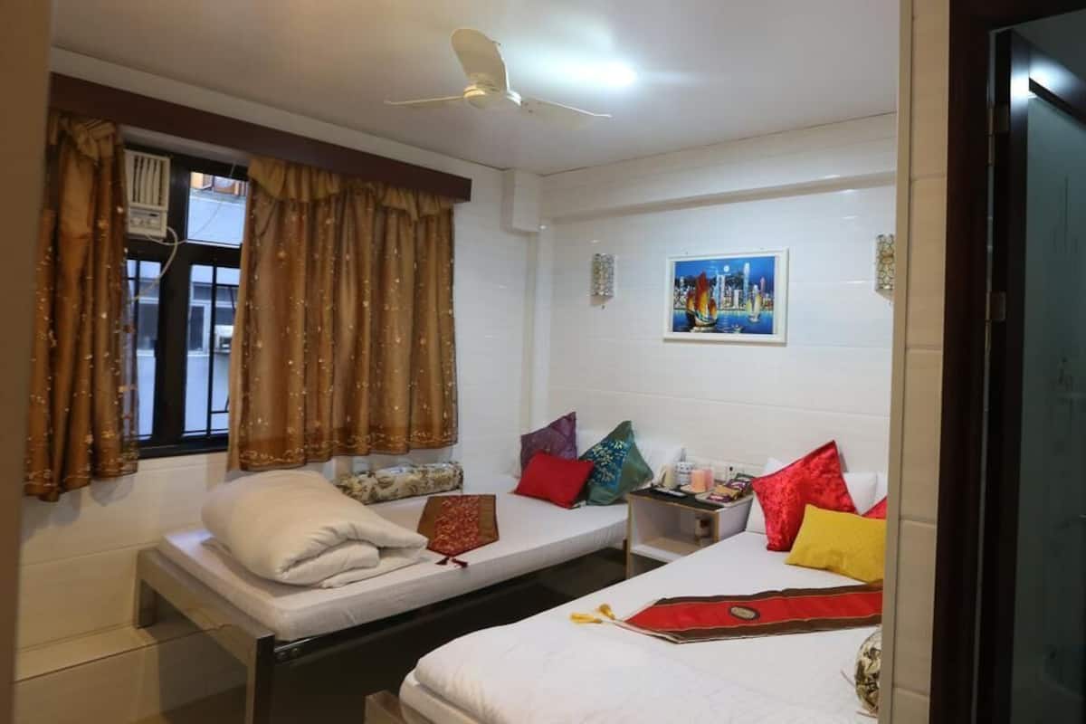 A room with two beds, a ceiling fan, a window with curtains, and a painting on the wall.