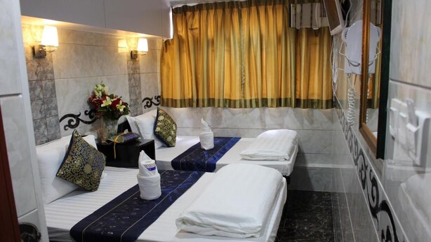 A hotel room with two beds, a marble wall, a curtain, and a small table with a vase of flowers. - Om Guest House (Kowloon)