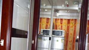 A corridor with tiled walls, a black and white tiled floor, and a microwave in the background. - Om Guest House (Kowloon)