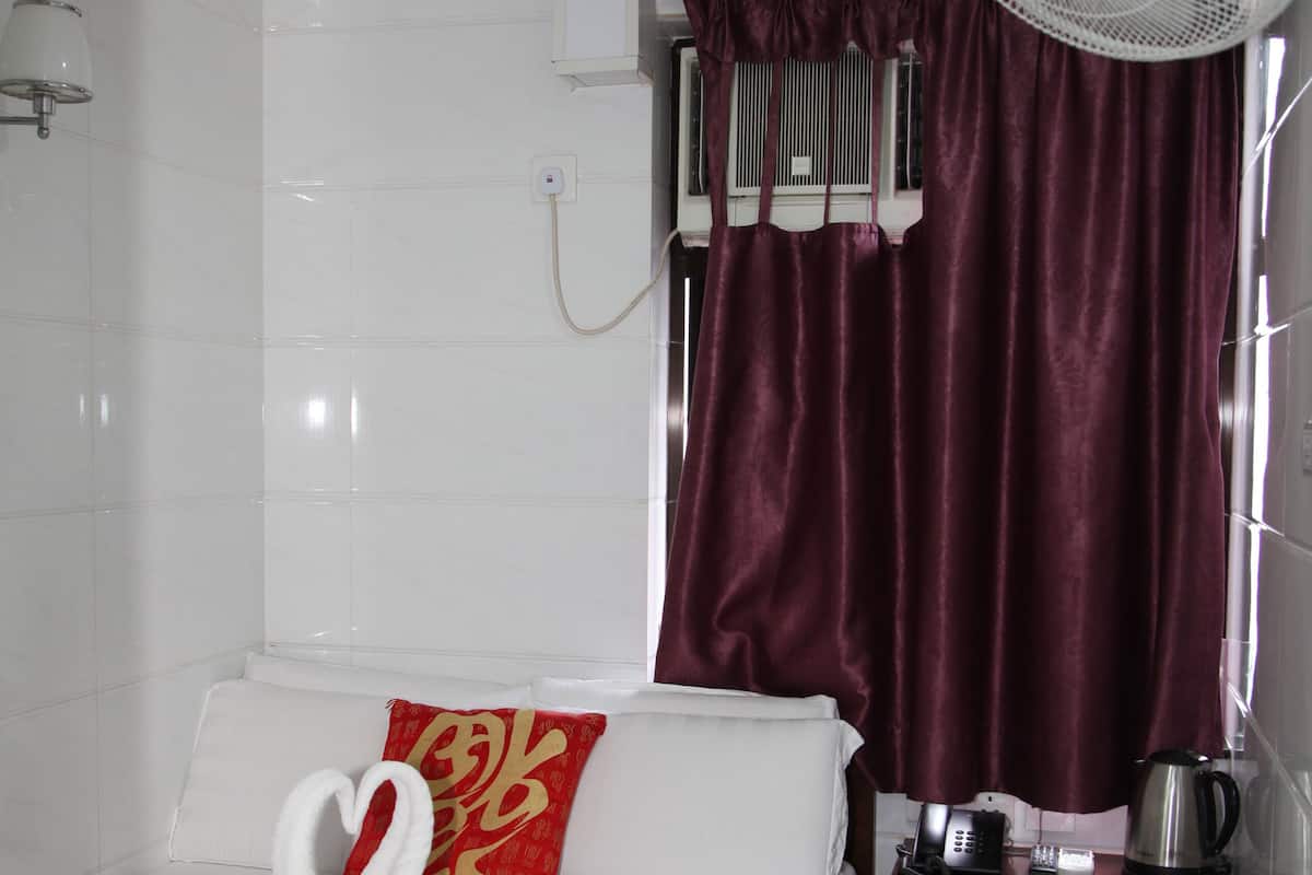 A hotel room with a bed, a fan, a coffee maker, and a window with curtains.