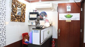 A reception area with a wooden door labeled "Strawberry Motel," a decorative mirror, a clock, and a small statue on a counter. - Om Guest House (Kowloon)