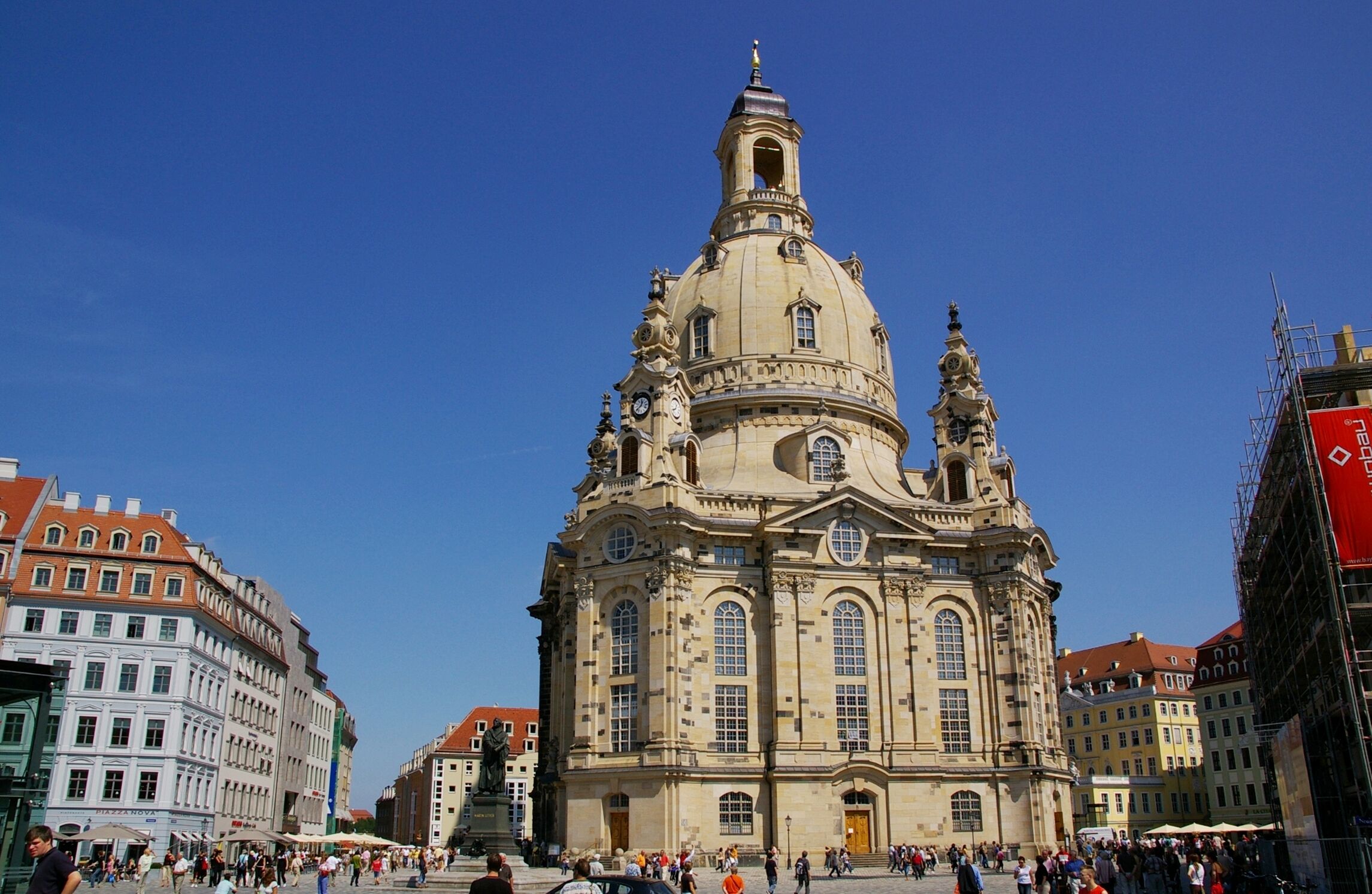 A historic building with a prominent dome and clock tower, surrounded by a bustling square with pedestrians.