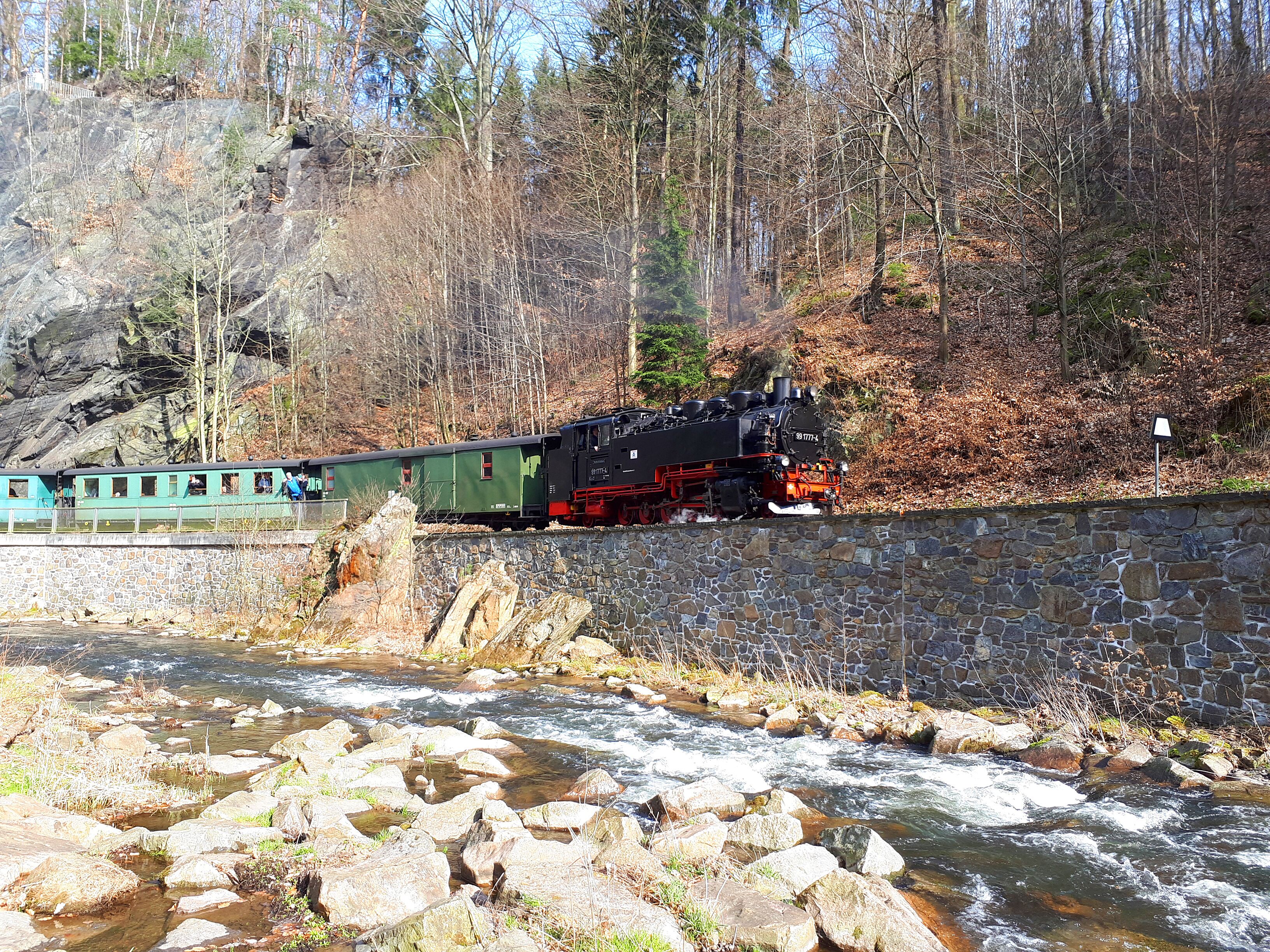 Een trein rijdt door een rotsachtig gebied met een rivier op de voorgrond.