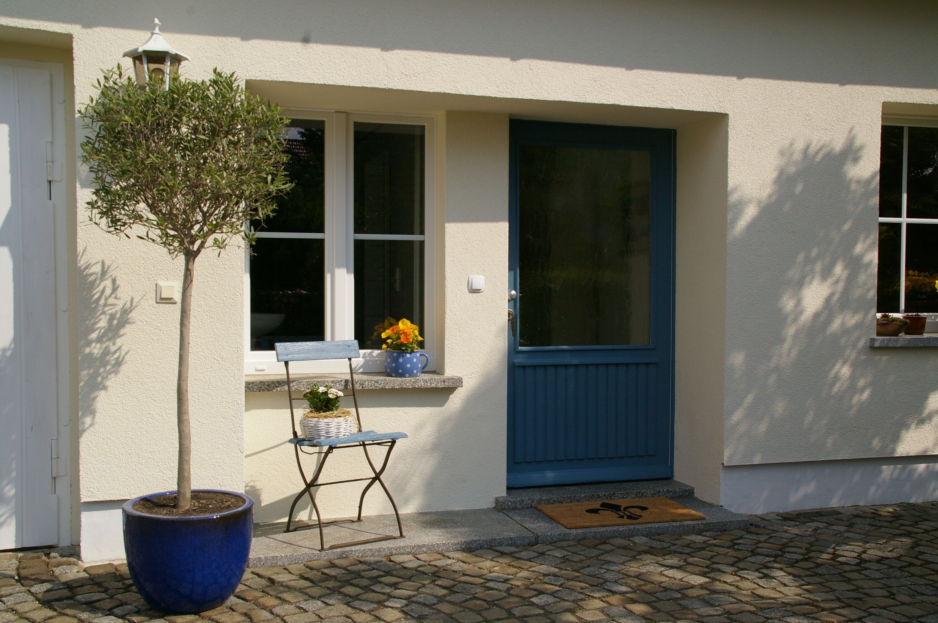 A house with a blue door, a potted tree, and a bench outside.