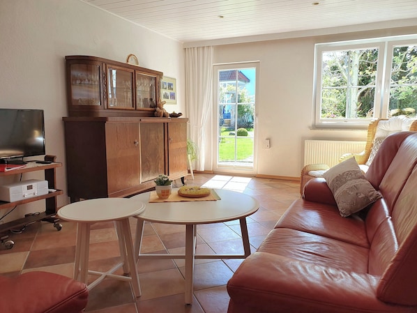 A living room with a leather sofa, a wooden cabinet with glass doors, a television, and a small table with a plant. - Rural holiday home amidst nature near Dresden (Laußnitz)