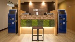 A reception area with a wooden counter, two ATMs, and a green wall feature. - Super Hotel Miyazaki (Miyazaki)
