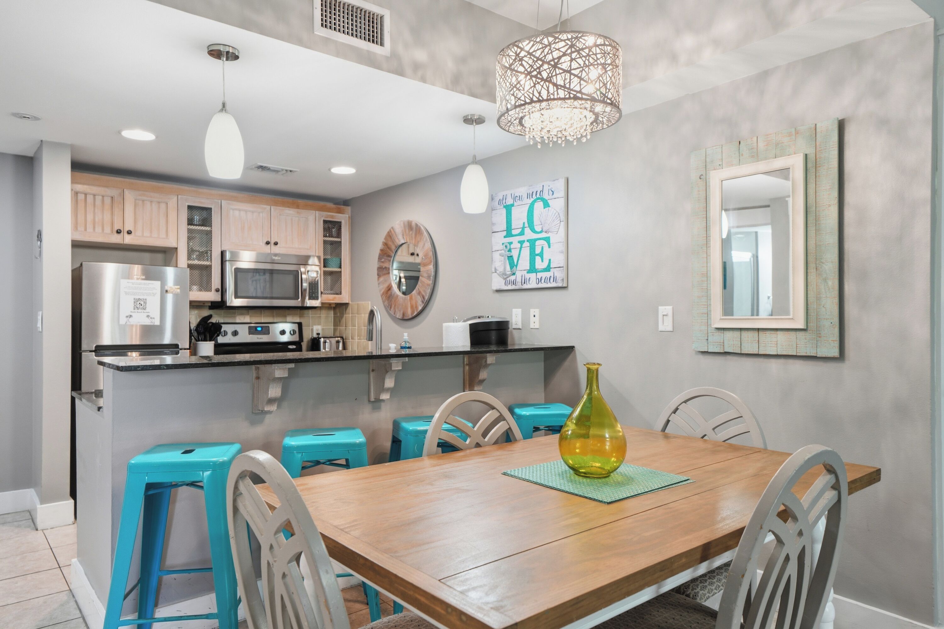 A modern kitchen with stainless steel appliances, a wooden dining table, and teal bar stools.