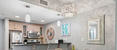 A modern kitchen with stainless steel appliances, a wooden dining table, and teal bar stools.
