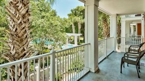 A covered outdoor area with a white railing, a palm tree, and a pool in the background. - Beautiful views overlooking the pool & hot tub (Miramar Beach)