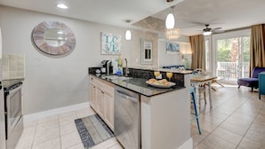 A modern kitchen with a central island, a dining area with a table and chairs, and a view of the outdoors through large windows. - Beautiful views overlooking the pool & hot tub (Miramar Beach)