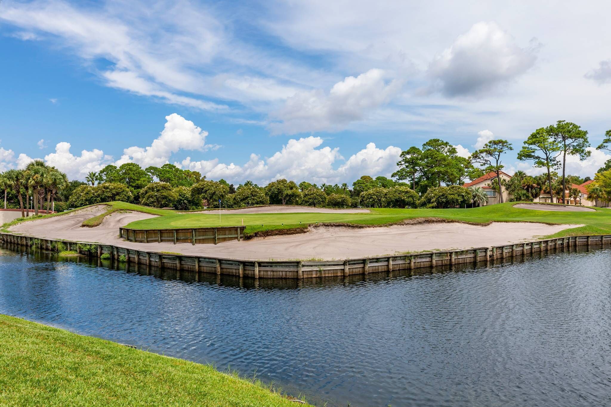 A golf course with a water body, green fairways, sand bunkers, and a clubhouse.