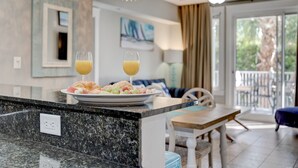 A kitchen counter with a plate of food and two glasses of orange juice. There is a dining area with a table and chairs, and a view of the outdoors through a glass door. - Beautiful views overlooking the pool & hot tub (Miramar Beach)