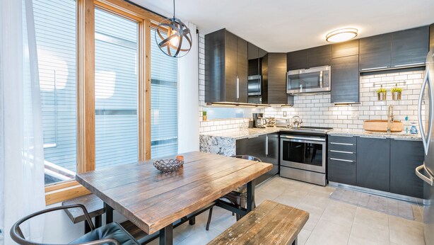 A modern kitchen with dark cabinetry, stainless steel appliances, and a wooden dining table. - Beautiful park like setting- Telluride Lodge Condo  (Telluride)