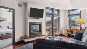 A modern living room with a sofa, a flat-screen TV, a fireplace, and a desk with a lamp.