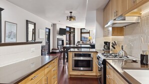 A modern kitchen with wooden cabinets, a central island with a stove, and a dining area with bar stools.