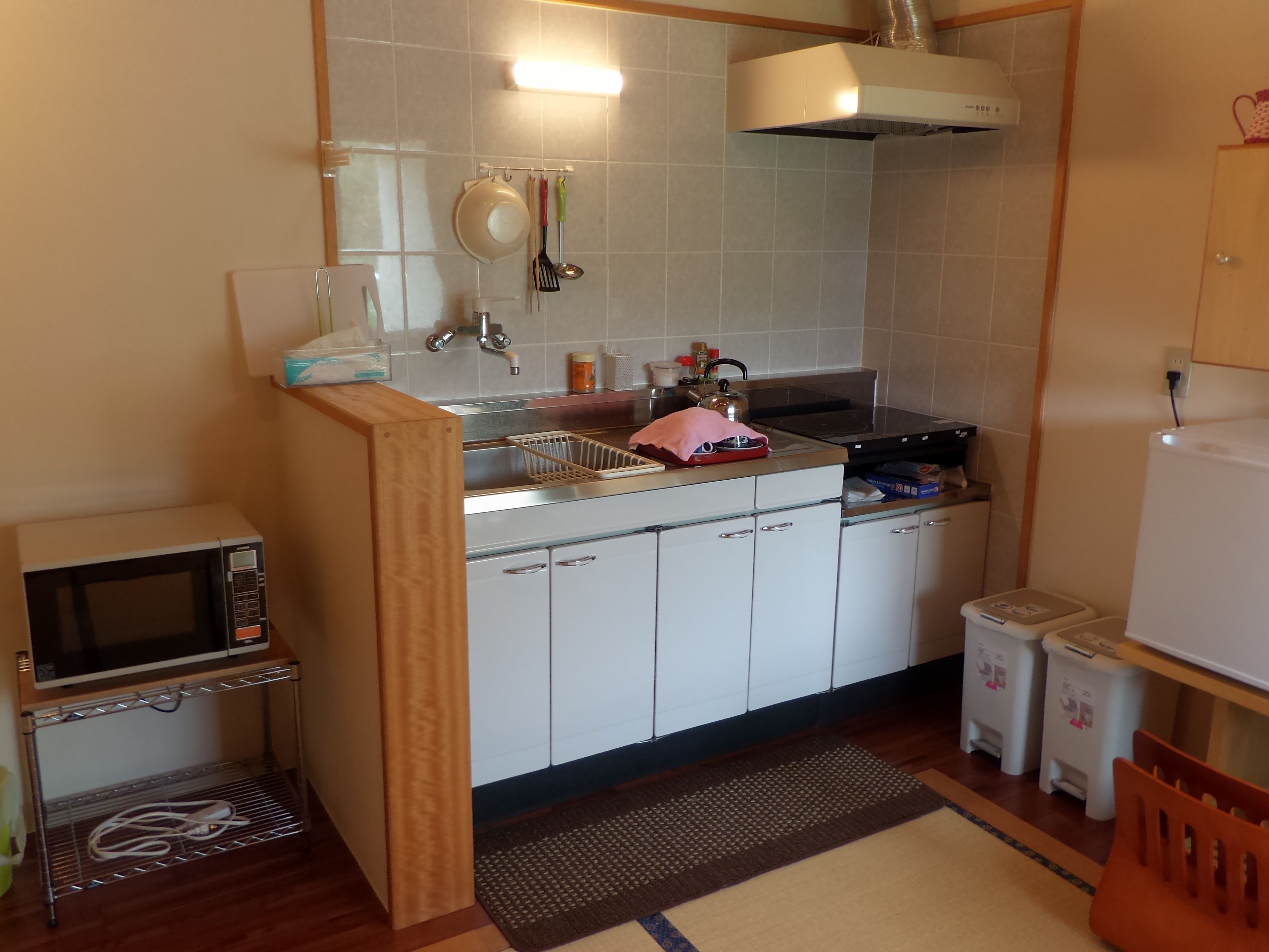 A compact kitchen with white cabinets, a microwave, a kettle, and a sink.