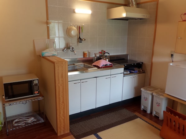 Una cocina compacta con gabinetes blancos, un microondas, una tetera y un lavamanos.