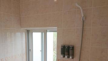 Een badkamer met beige tegels, een glazen deur, een douche en twee zeepdispensers.