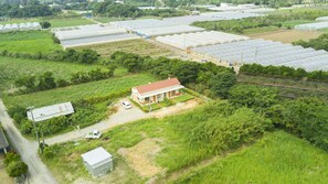 A large greenhouse complex with multiple rows of greenhouses, a small house with a red roof, and a white truck parked nearby. - Kaeruya (Nakijin)
