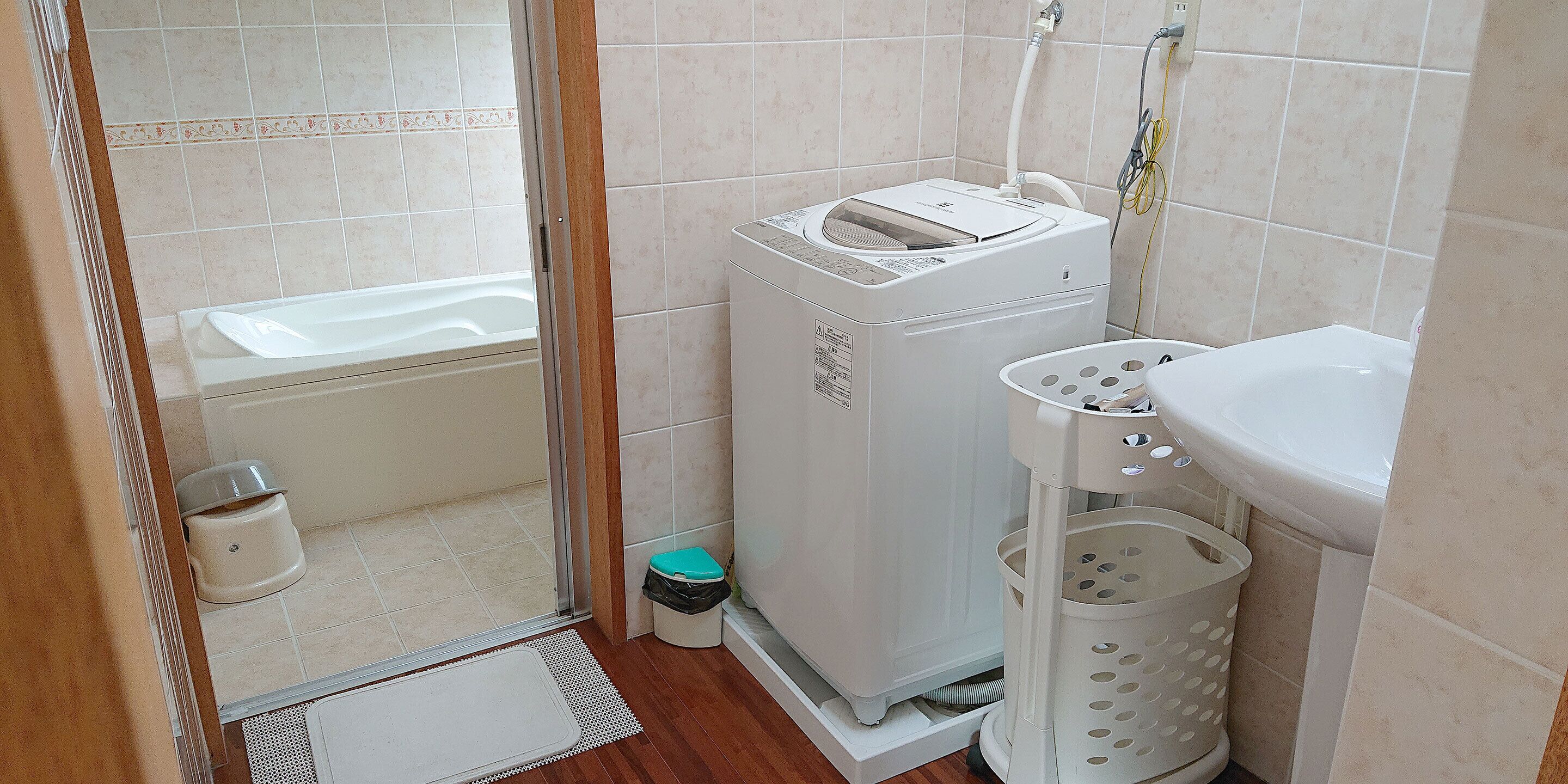 A small bathroom with a white sink, a washing machine, a toilet, and a shower area.