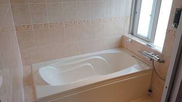 A bathroom with a bathtub, a window, and a shower.