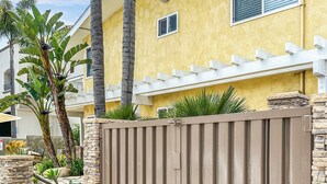 A gated residential area with a yellow house, palm trees, and a stone wall. - Prime Beachside Stay – Unbeatable Location #8 (Carlsbad)